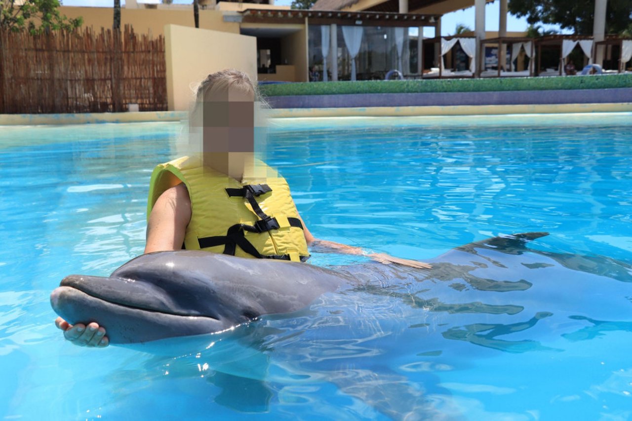 a_tourist_holding_a_dolphin_in_water_at_a_tourist_attraction_in_mexico