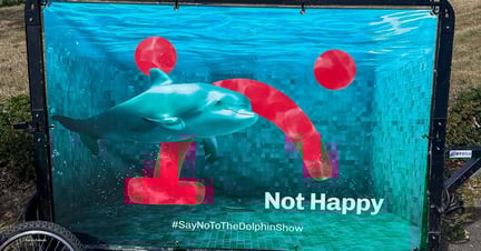 An LED bike sign used for the TUI Hannover protest, in collaboration with 21 animal welfare NGOs. Image shows the TUI logo flipped to display an unhappy face, with a captive dolphin in a small tank. Text reads: Not Happy. #SayNoToTheDolphinShow